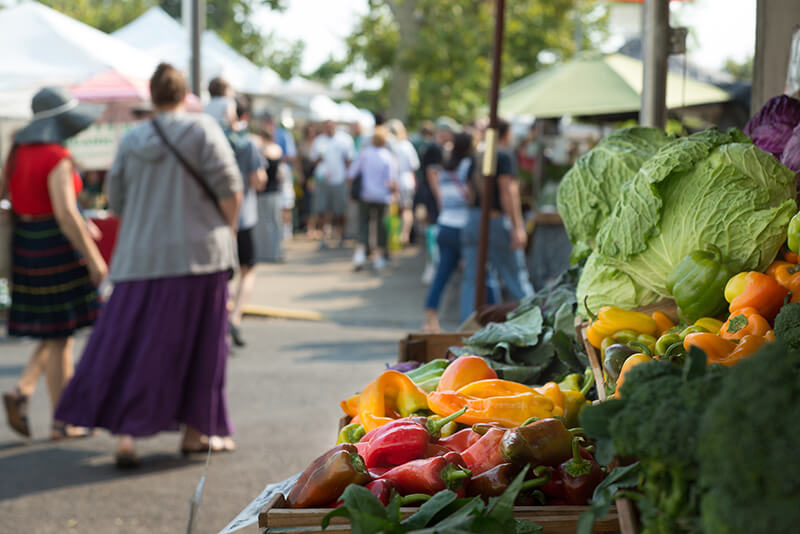 A crowd of people walking past fresh produce stalls at the Liberty Hill farmer's market