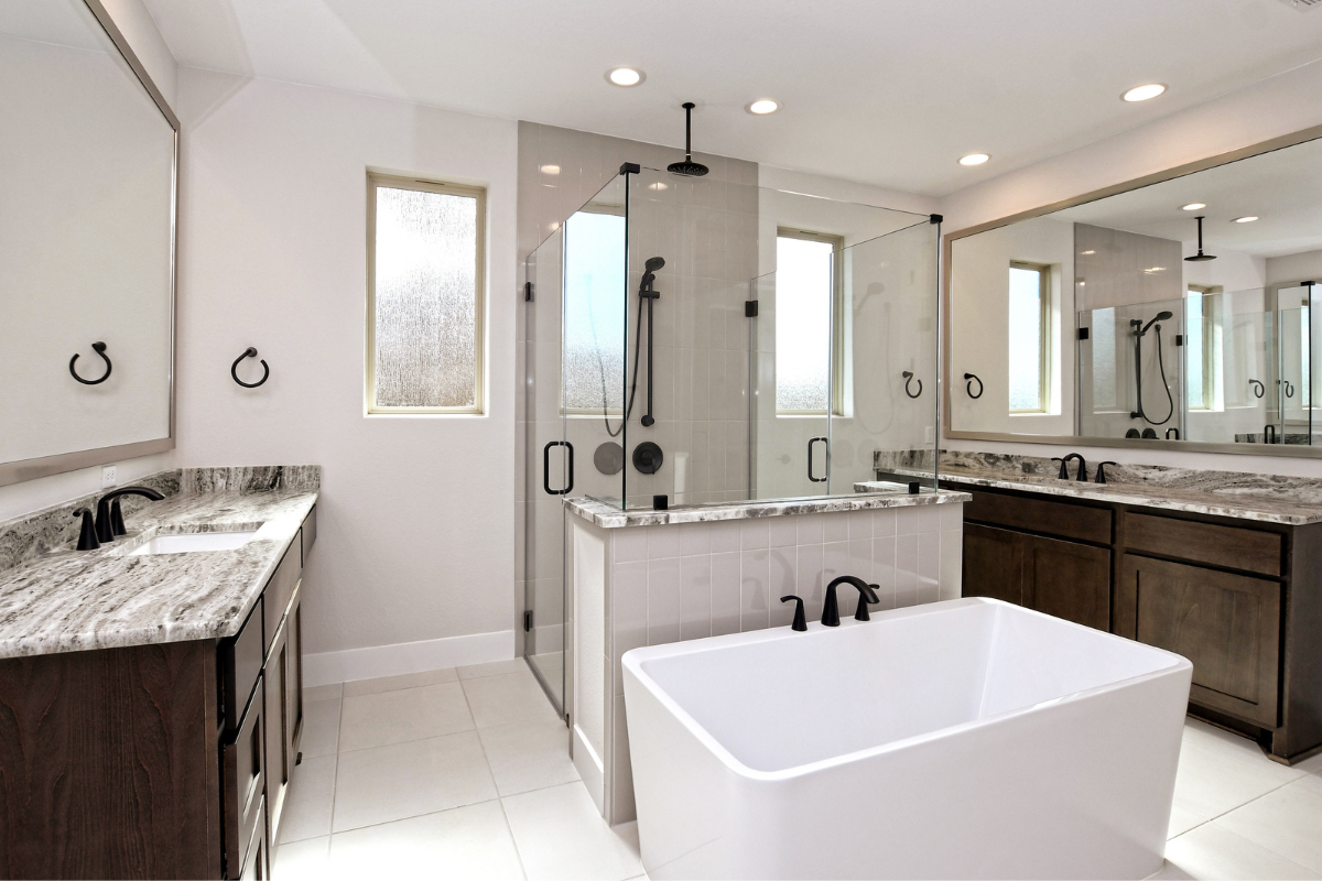 Interior bathroom image of the Emerald floorplan part of Giddens Homes' Gemstone Series. Features two sinks and a shower and tub in the middle. 