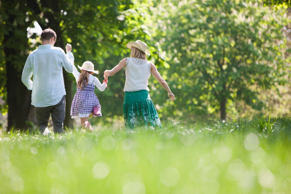 Family walking in a park surrounded by green grass and large trees. 